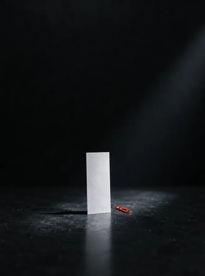 좁은 조명 아래 서 있는 빈 종이 한 장과 주황 클립